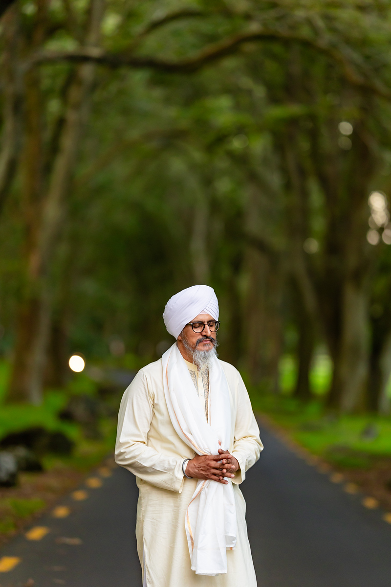 Bhai Yadvinder Singh Ji in deep meditative contemplation with hands folded in ardas, wearing traditional white dastaar and hazuriya in Auckland nature.