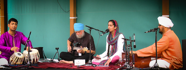 Live devotional stage photograph of Bhai Yadvinder Singh Ji leading harmonium accompaniment during the Sangat Kirtan Tour.
